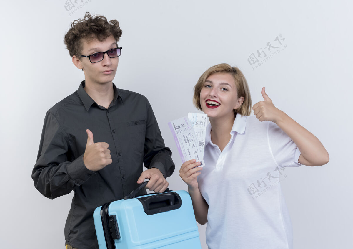游客一对幸福的年轻游客 一男一女拿着手提箱和机票 微笑着竖起大拇指站在白色的上空站立女人表演