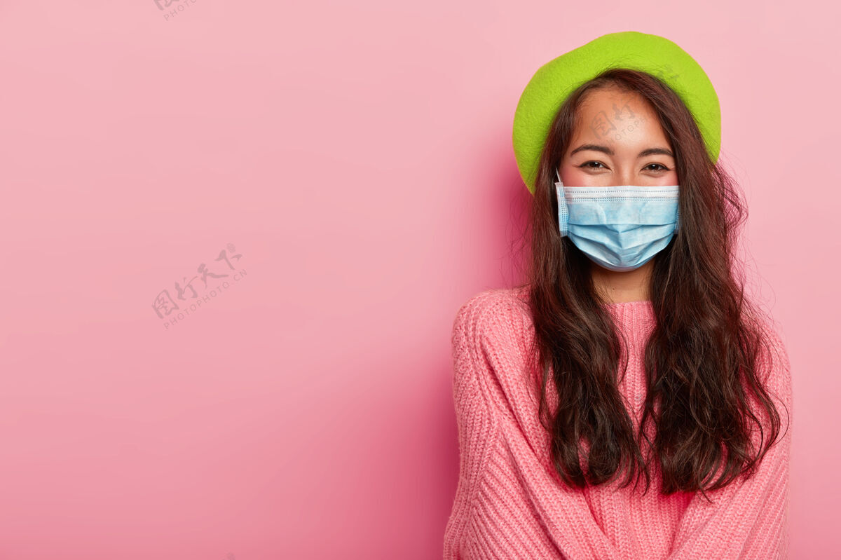 病毒女人戴着防病面具 戴着绿色贝雷帽和超大的粉色毛衣保健疼痛美容