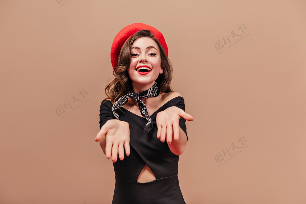 贝雷帽一位穿着黑色连衣裙 戴着红色帽子的迷人女士微笑着 露出了她的手掌成人女性卷发