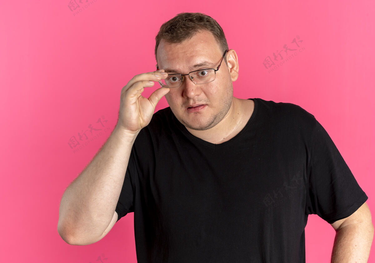 站一个戴眼镜的胖男人穿着黑色t恤 看着一件迷糊的东西T恤眼镜粉色