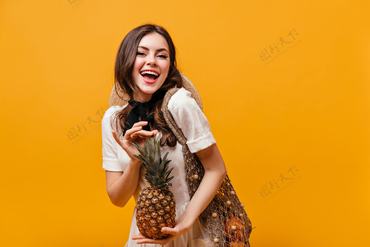 连衣裙穿着棉质夏装的女士笑着摆出橙色背景的菠萝和环保袋的姿势波浪发卷发头发