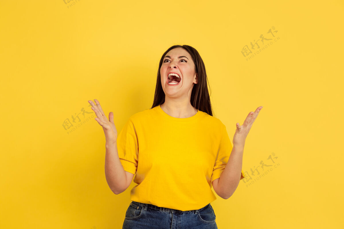 衬衫愤怒的尖叫隔离在黄色墙壁上的白种女人的肖像休闲风格的漂亮的黑发女性模特人类情感的概念 面部表情 销售 广告 复制空间高管半身女孩