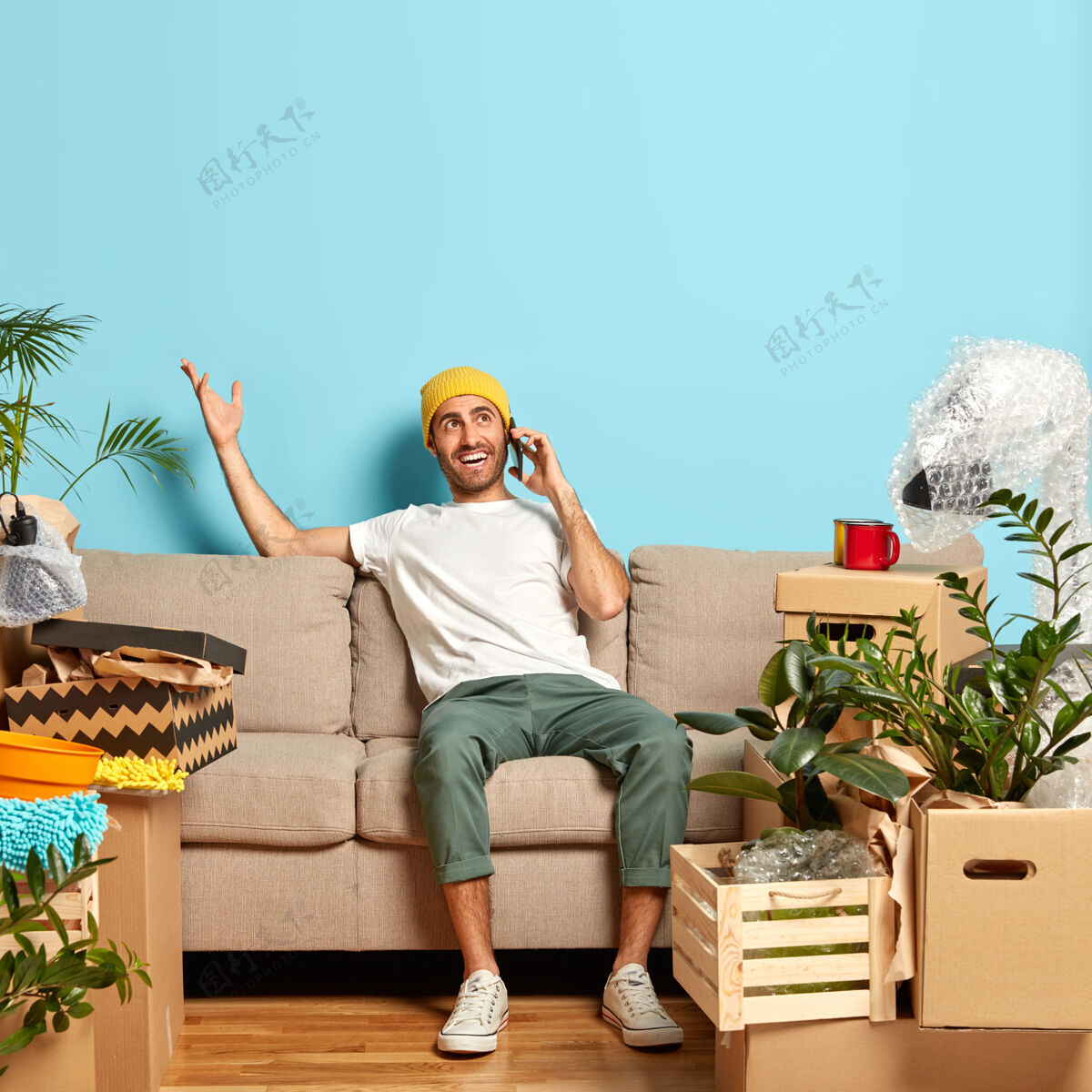 纸板画像中的快乐男人有电话交谈 用一只手做手势 试图解释去他新公寓的路线戴着黄色的帽子房地产手机复制空间