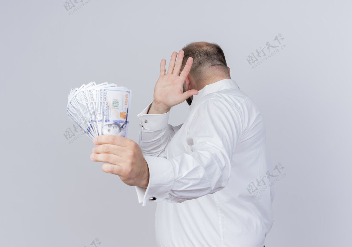 戴着一个留着胡子的男人穿着白衬衫 手里拿着现金 站在白墙上用手抵着钱做防御手势握着钱胡须