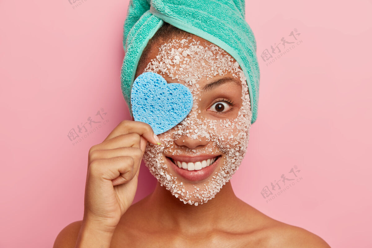 裸体开朗的年轻女子用心形化妆棉捂住一只眼睛 卸妆 用海盐擦洗脸部 温柔的微笑人类室内肩