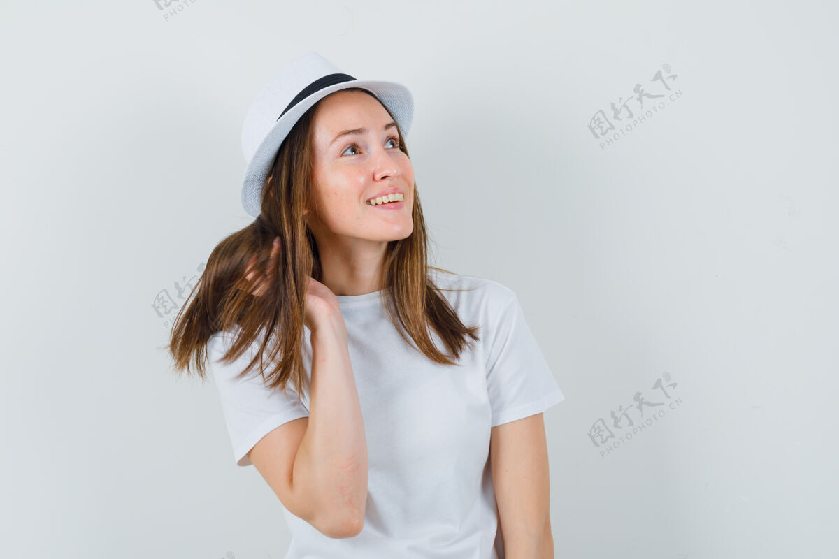 年轻年轻女孩一边摆姿势一边抬头看 穿着白色t恤 戴着帽子 看上去很华丽 正前方的景色积极而童年