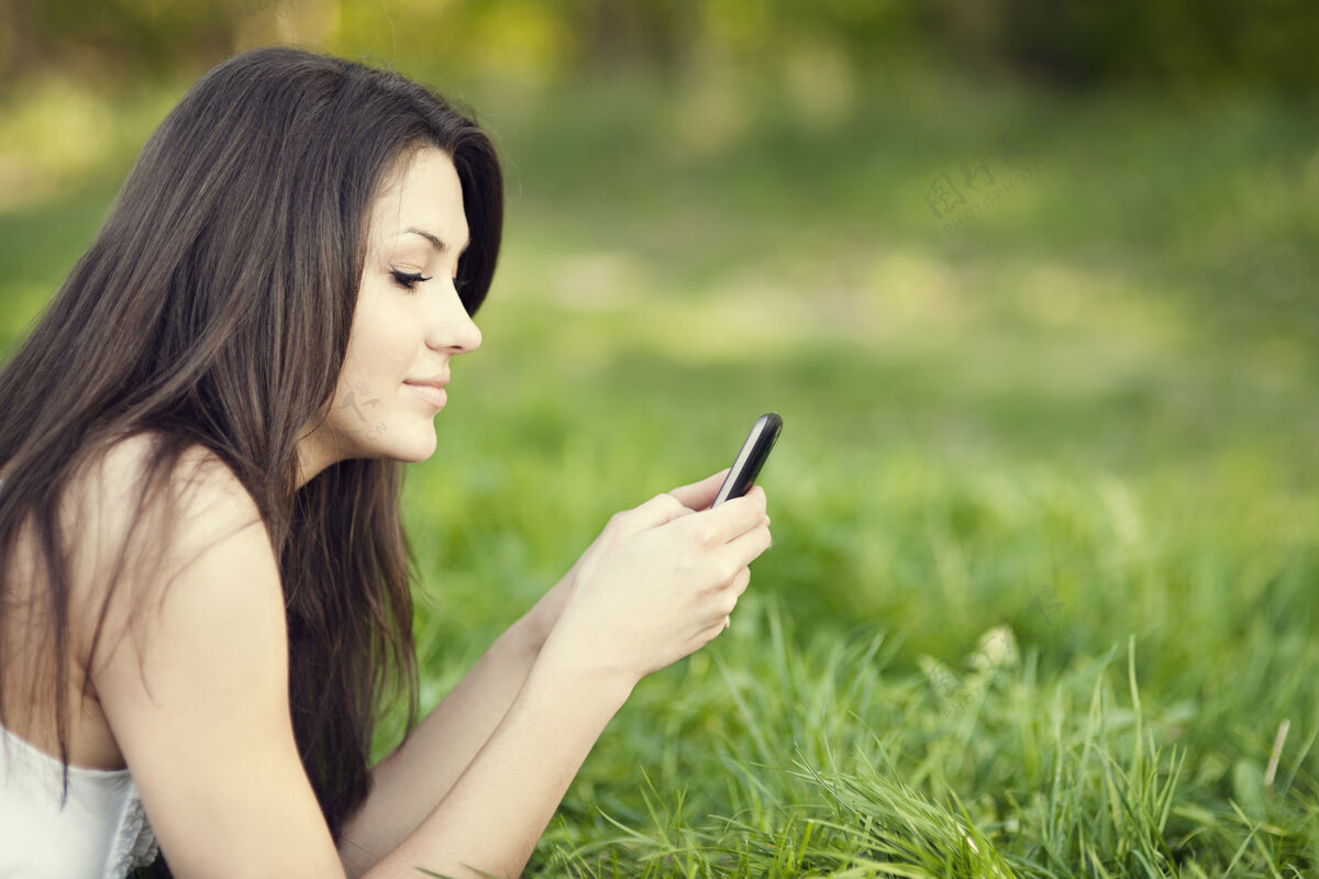 躺下在草地上发短信的年轻女人头和肩膀互联网激情
