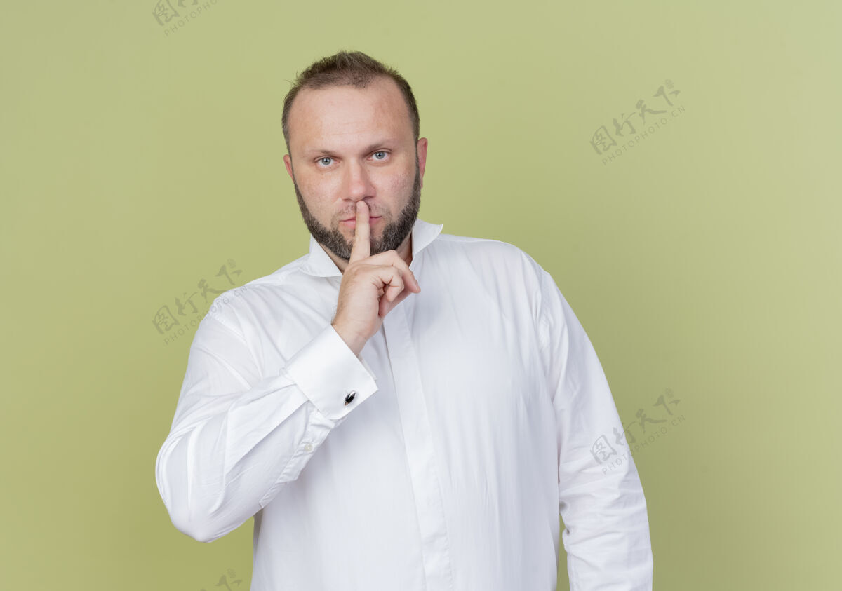 手势一个留着胡子的男人 穿着白衬衫 手指放在嘴唇上 站在轻墙上做着沉默的手势沉默手指男人