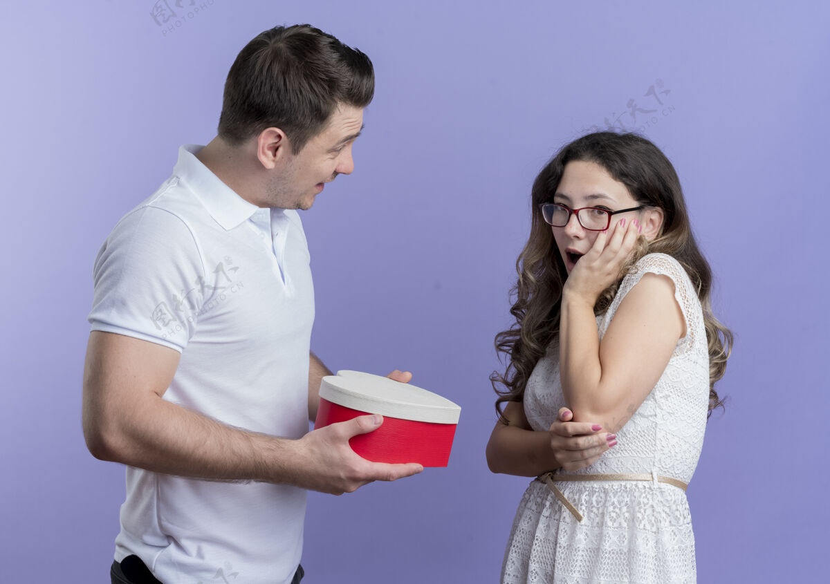 给予一对年轻的情侣站在蓝色的墙上给他心爱的女友一个礼物盒年轻站着情侣