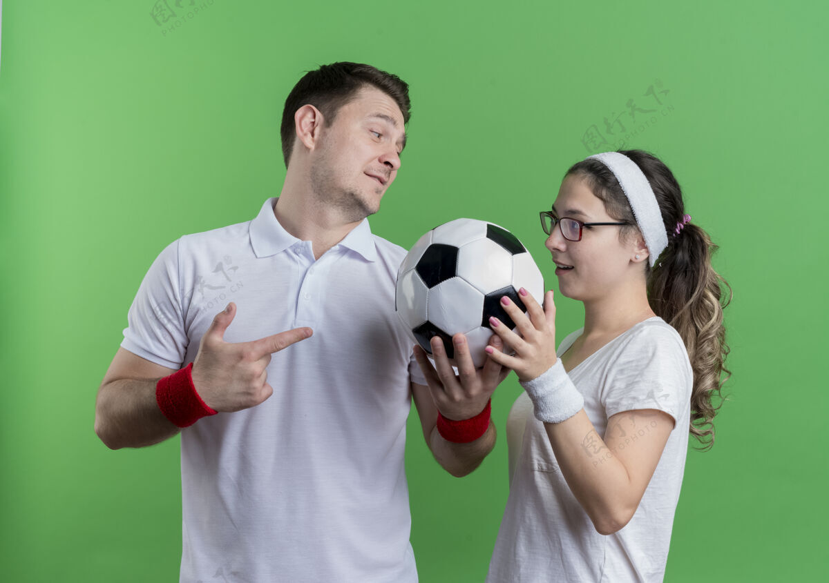 年轻一对年轻的运动情侣站在一起 手里拿着足球越过绿墙抱着每个足球