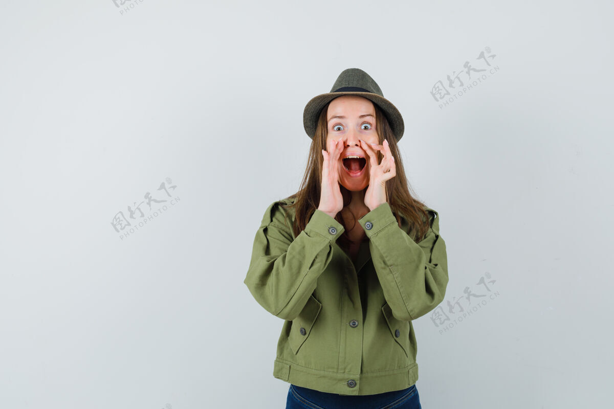 年轻年轻女性在夹克 裤子 帽子前视图中用手靠近张口讲述秘密肖像开放黑发