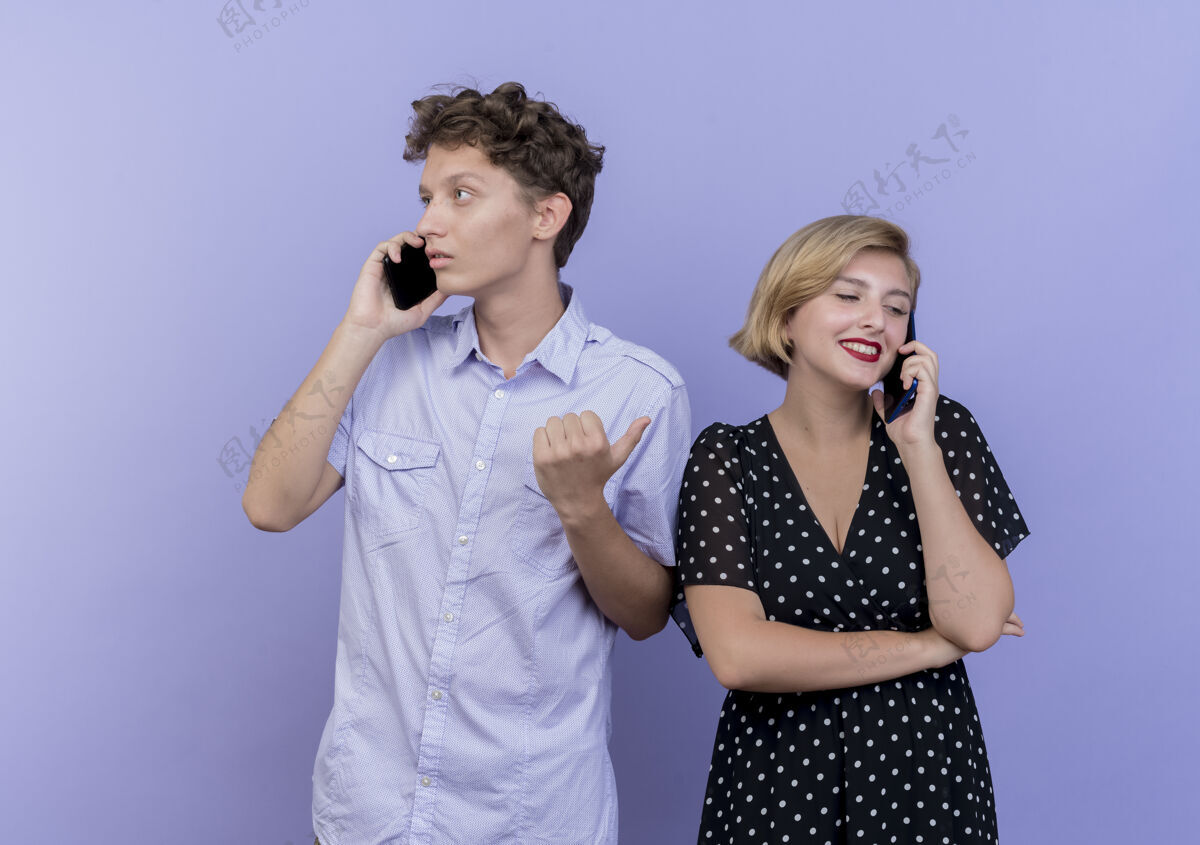 聊天年轻漂亮的夫妇站在蓝色的墙上用手机交谈情侣手机女人