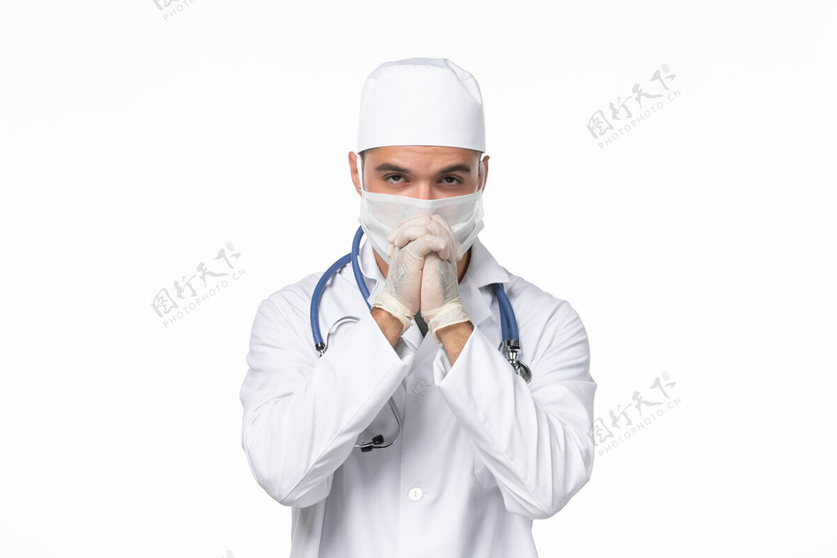 专业正面图：男医生穿着医疗服 戴着口罩 在白色墙壁上摆姿势 传染疾病医疗冠状病毒预防冠状病毒防护