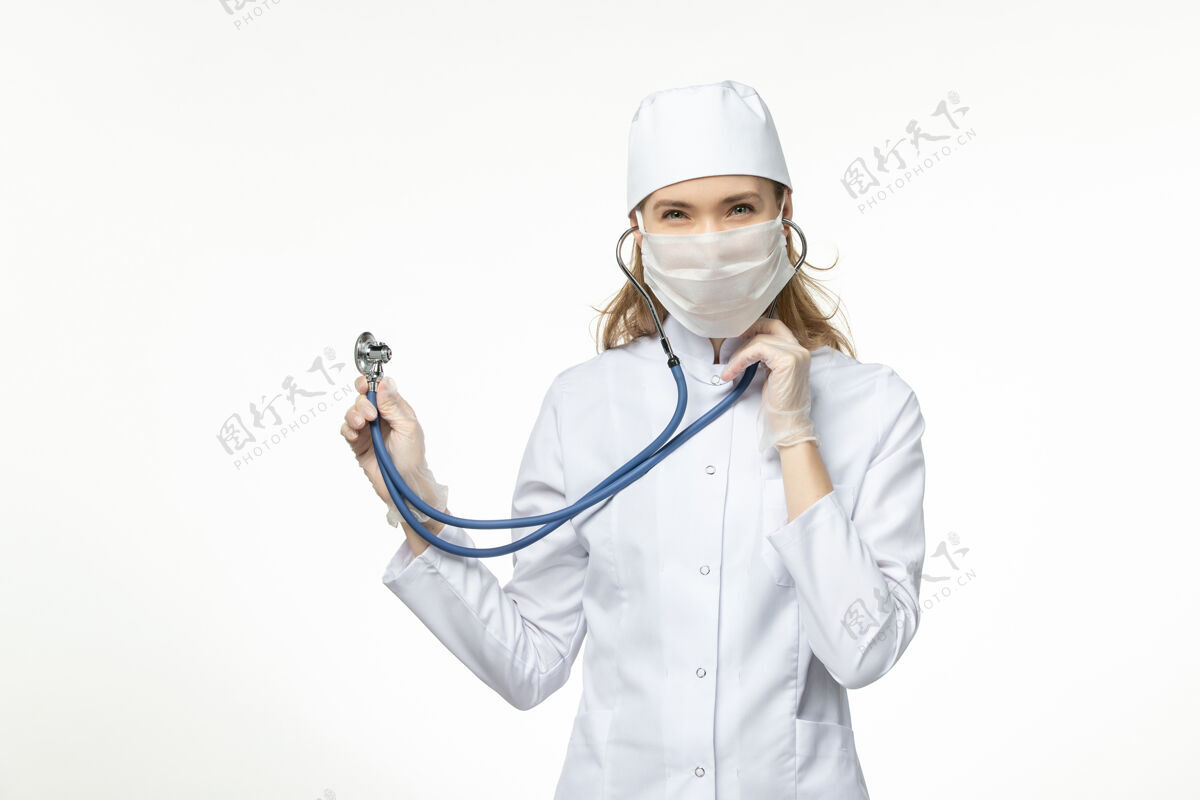 套装正面图女医生穿着白色医疗服 带无菌口罩 因冠状病毒使用听诊器对白墙疾病大流行性疾病冠状病毒-听诊器疾病冠状病毒预防
