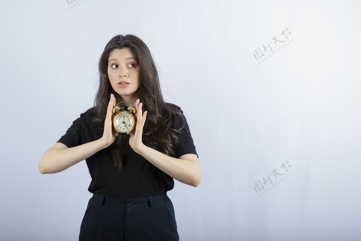 计时器黑发女孩的肖像 穿着黑色的衣服 拿着钟 摆着灰色的姿势快工作年轻