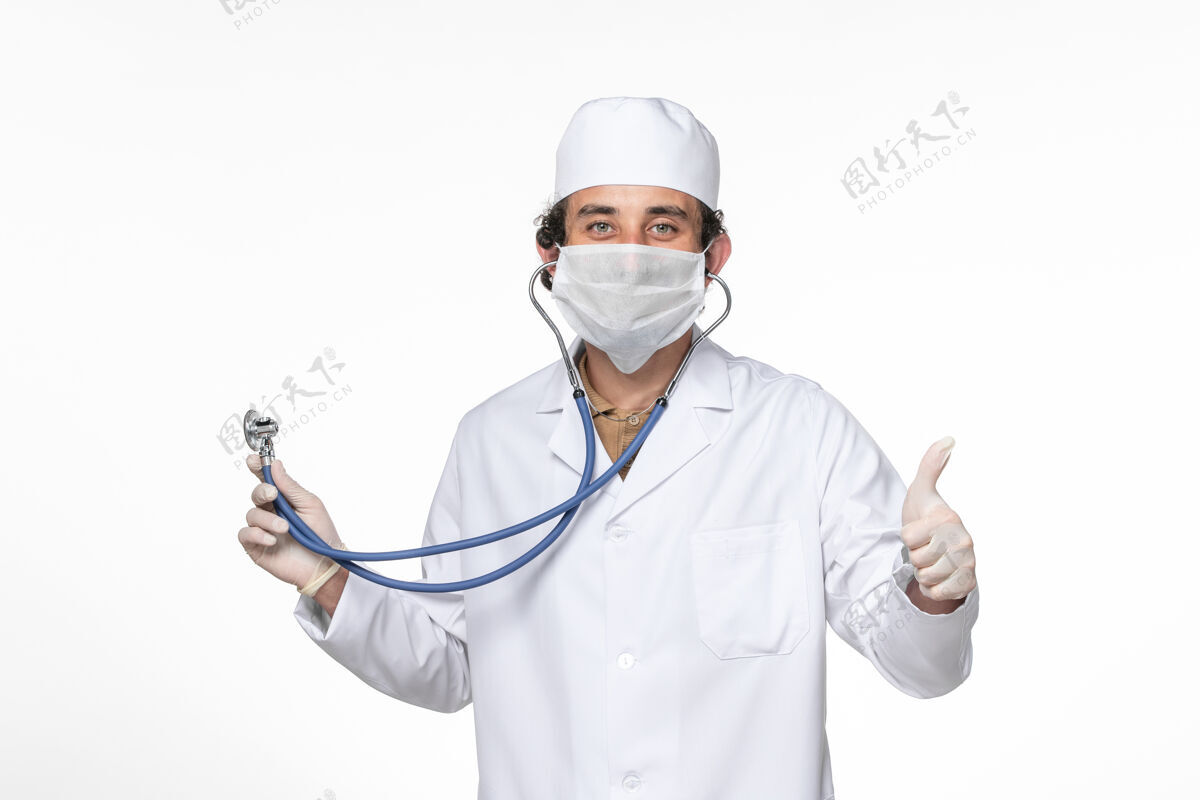 医生正面图：男医生穿着医疗服 戴着口罩 用听诊器在白墙飞溅的冠状病毒大流行中保护自己不受感染外套听诊器正面