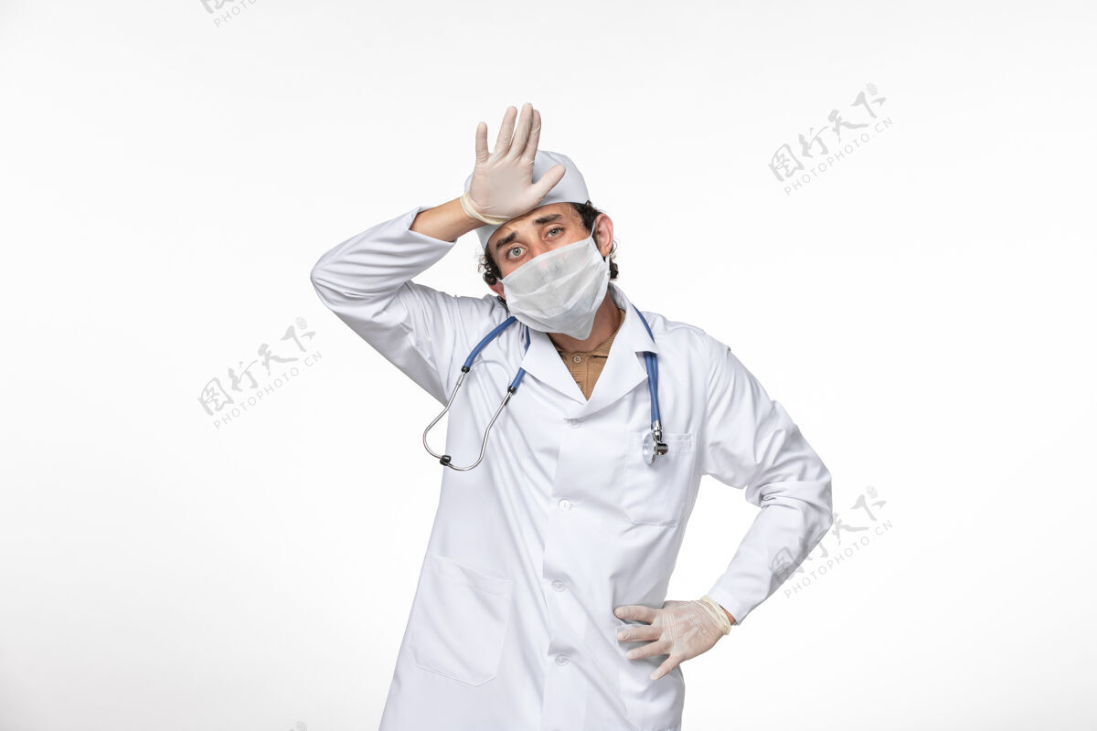 冠状病毒正面图：男医生穿着医疗服 戴着无菌口罩 以防冠状病毒在浅白的墙壁上飞溅 引起冠状病毒大流行专业查看防护