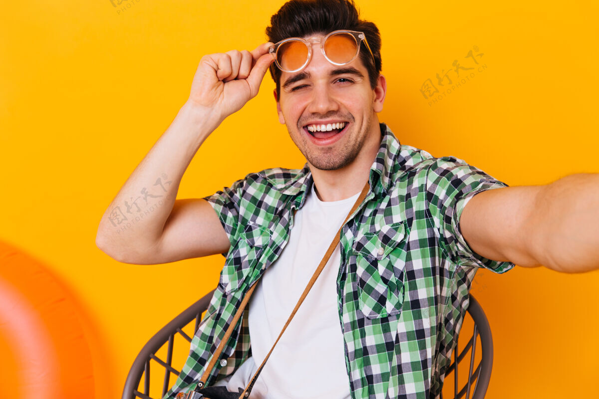 太阳镜穿着白色t恤和格子衬衫的帅哥摘下眼镜 眨眨眼 在橙色的空间里自拍深色电话信心