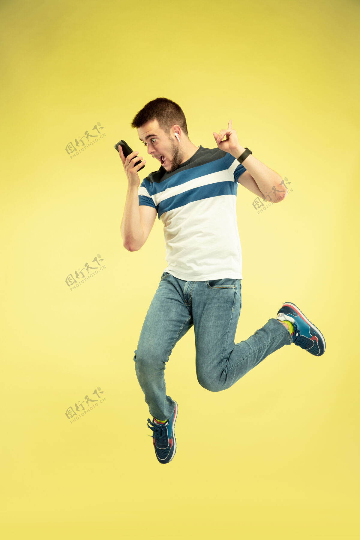 平板电脑黄色背景上有小玩意的快乐跳跃人的全长肖像设备积极运动