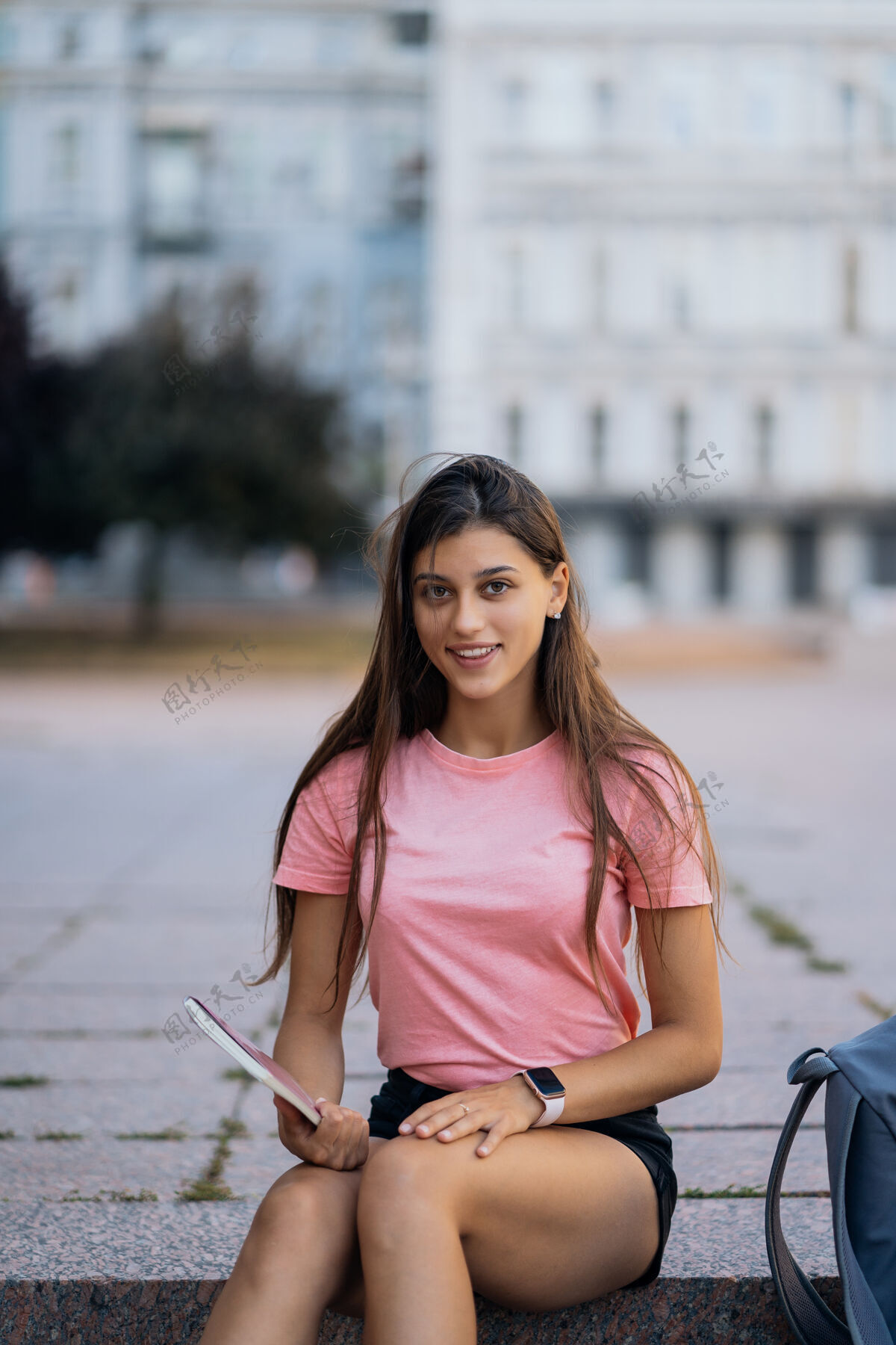 户外快乐的年轻女子坐在街上的台阶上做笔记教育背包街道