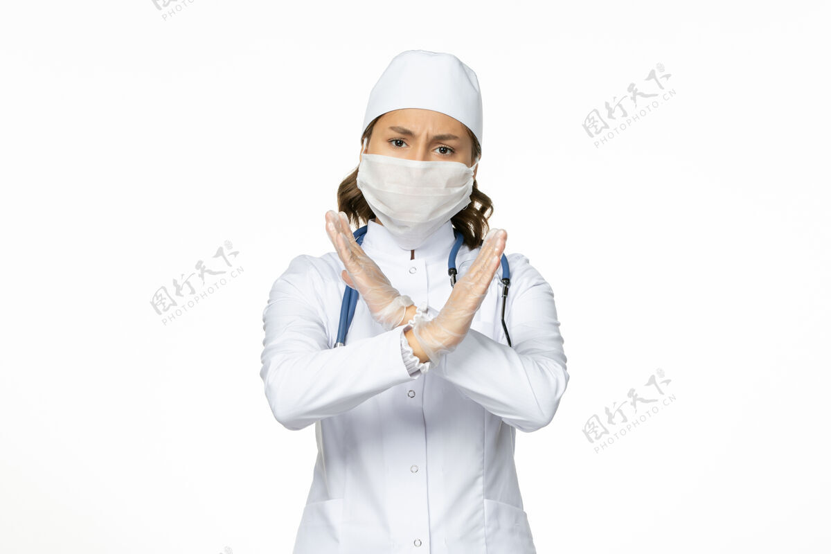成人正面图女医生穿着白色医疗服 戴着口罩 因白墙上有冠状病毒大流行性疾病隔离冠状病毒面罩医生视图
