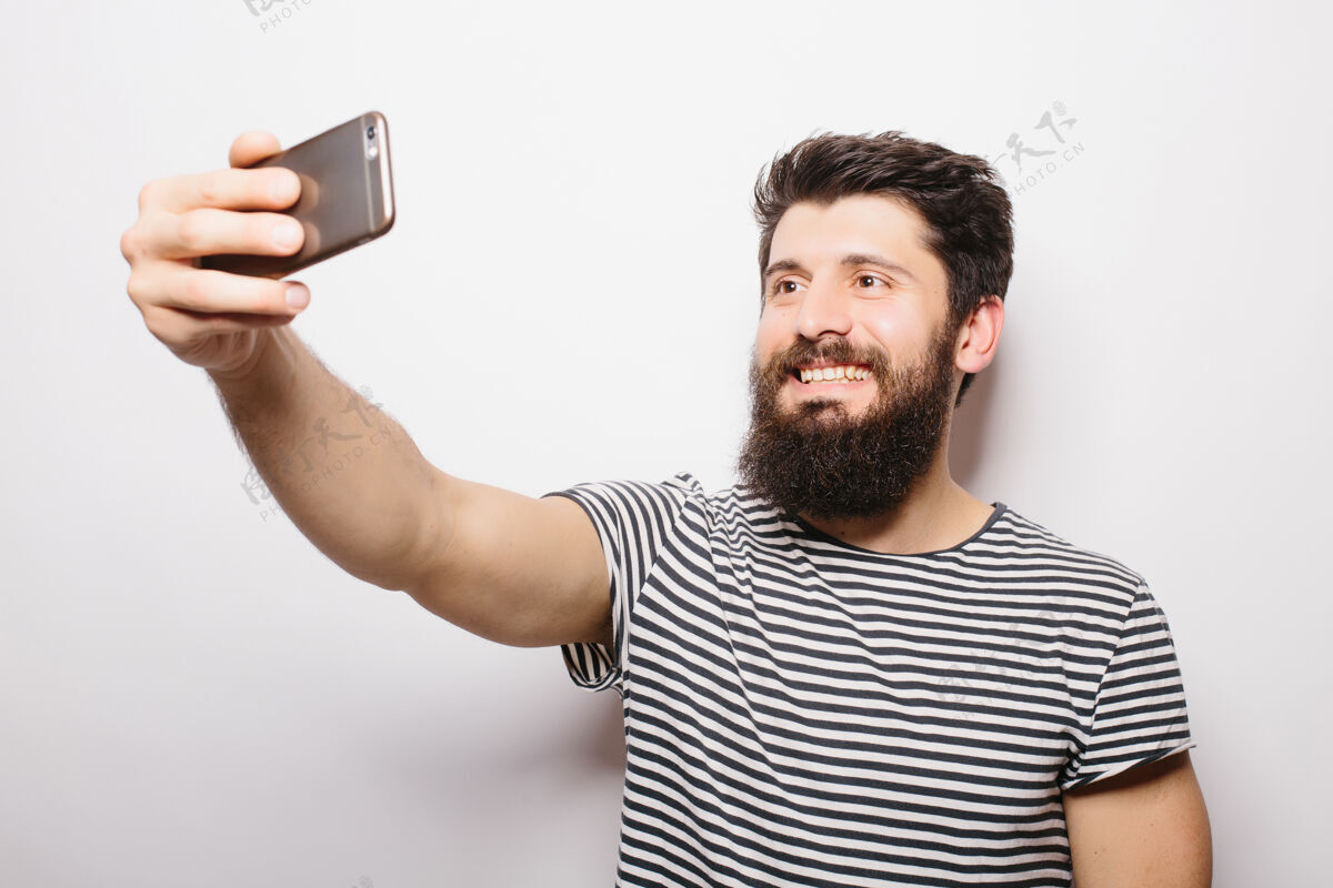 未保存一个开朗随意的男人在智能手机上自拍的照片被隔离在白色的墙上抱着拍摄站着