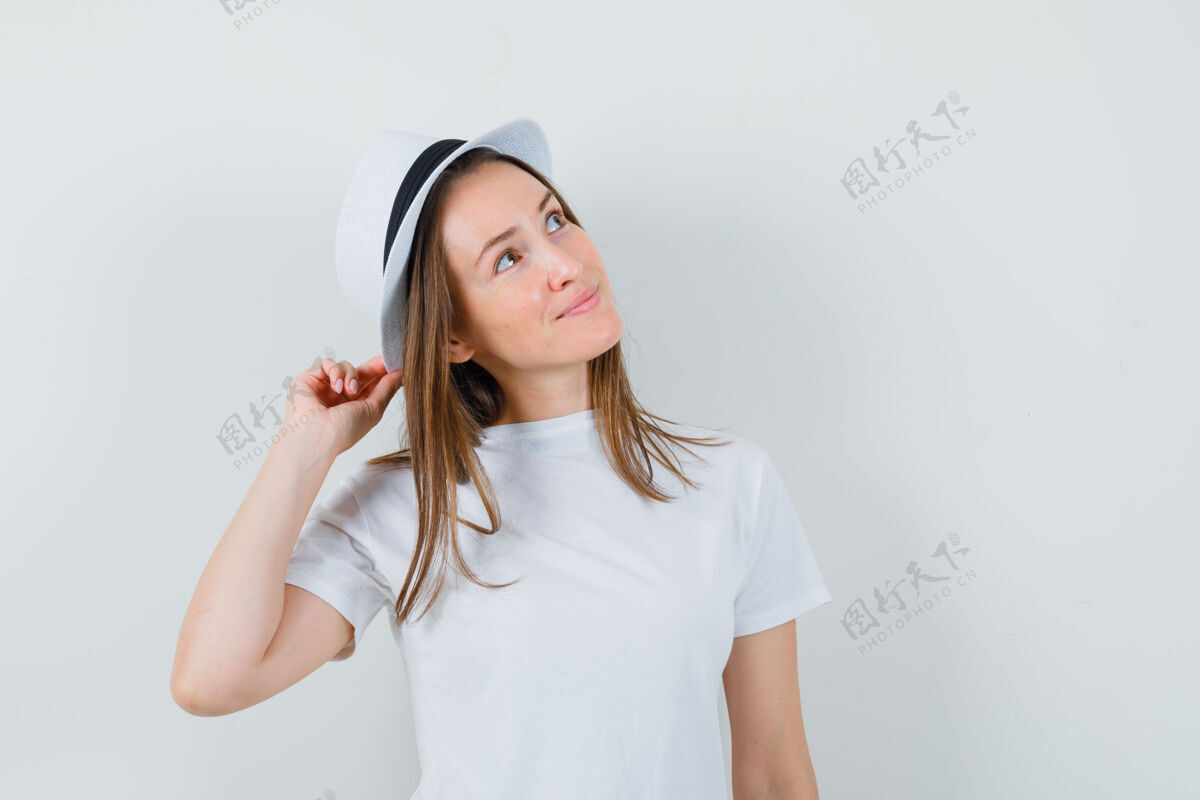 积极年轻女孩拿着帽子 穿着白色t恤抬头望去 看起来很梦幻前视图女人快乐小