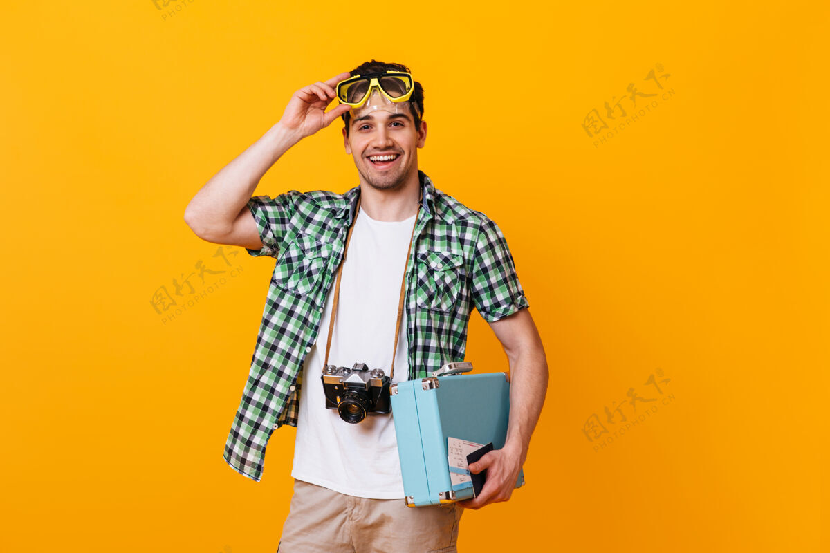 冒险在橙色的空间里 一个穿着夏装的开朗男人摘下了潜水面具游客们拿着复古相机和蓝色手提箱摆姿势老式相机采取手提箱