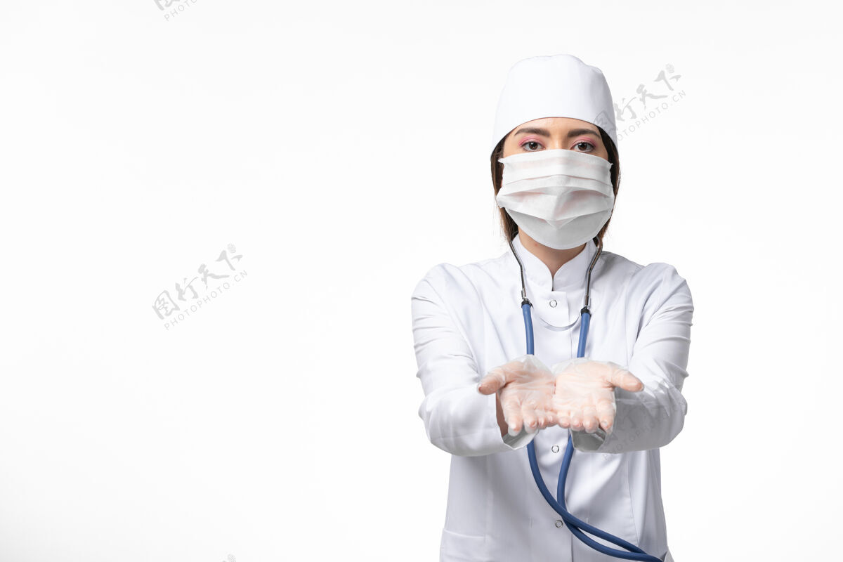 正面正面图女医生穿着白色医疗服 戴着口罩 因白墙上大流行疾病 医学病毒大流行 病毒共价药品大流行听诊器