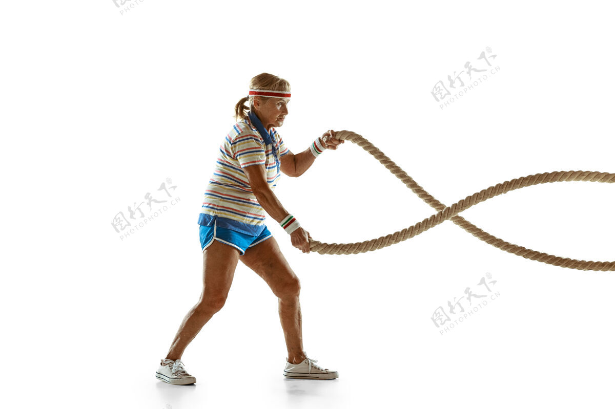 爱好穿运动服在白墙上用绳子训练的高级女子乐趣玩快乐