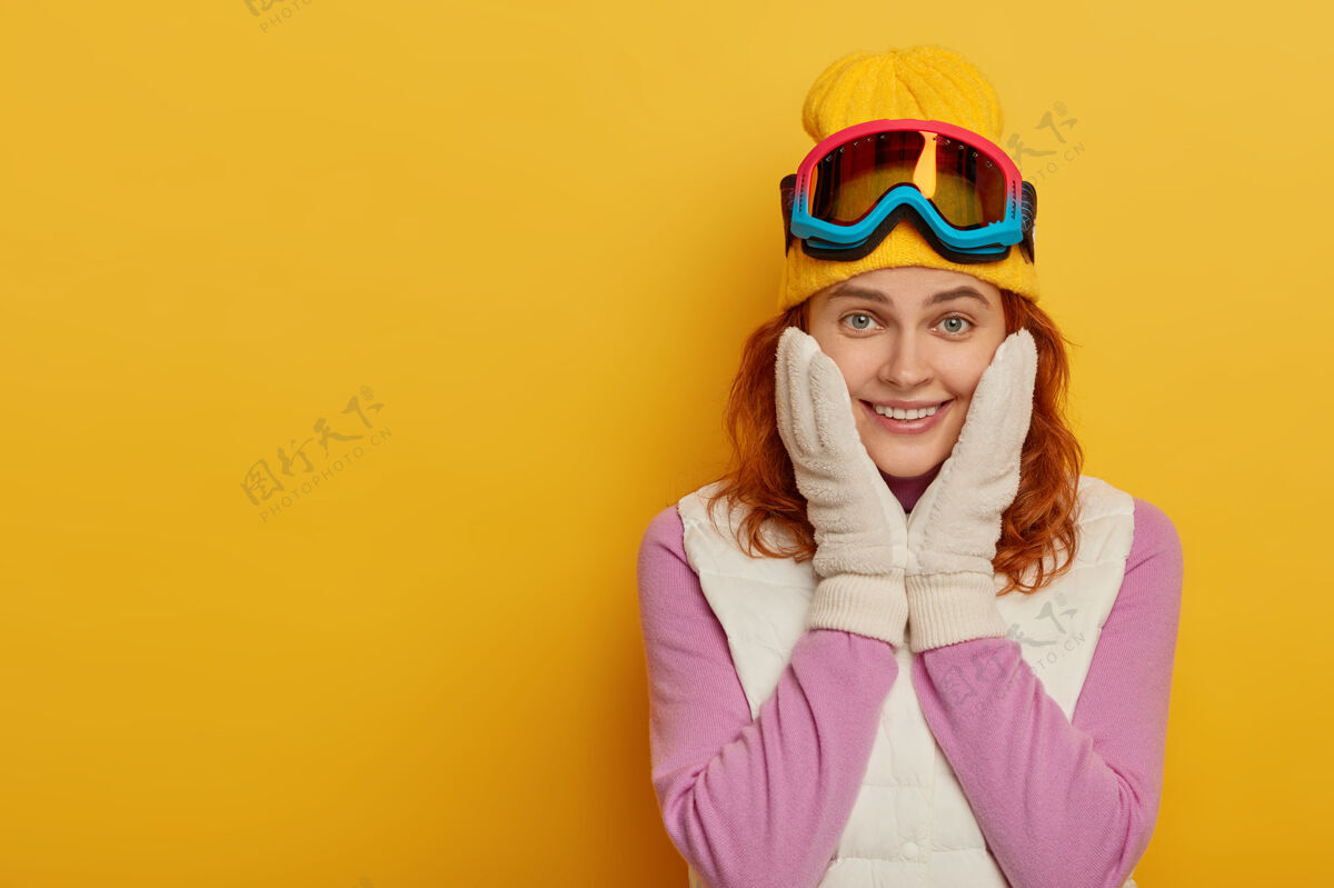 运动装笑容可掬的红发滑雪女孩有着幸福的表情 抚摸着脸颊 隔离在黄色的背景下牙齿肖像年轻