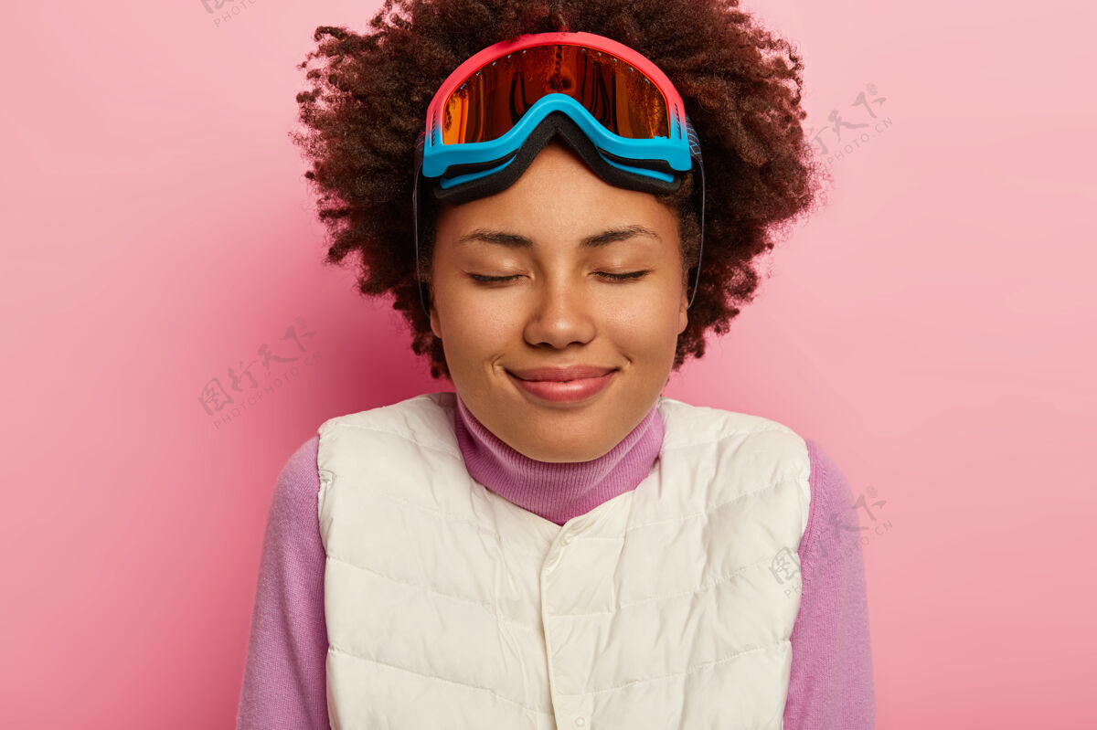 罗西特写照片中快乐的女滑雪者穿着白色背心 戴着滑雪眼镜 留着卷发白色面具冬天