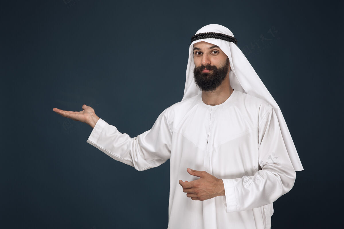 东方深蓝色空间上的阿拉伯沙特男子半身像年轻男模微笑着指着指向围巾意外