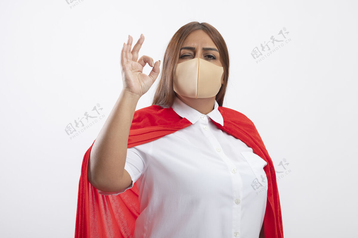 手势高兴的中年女超人戴着医用口罩 表情很好 隔离在白色上女性穿超级英雄