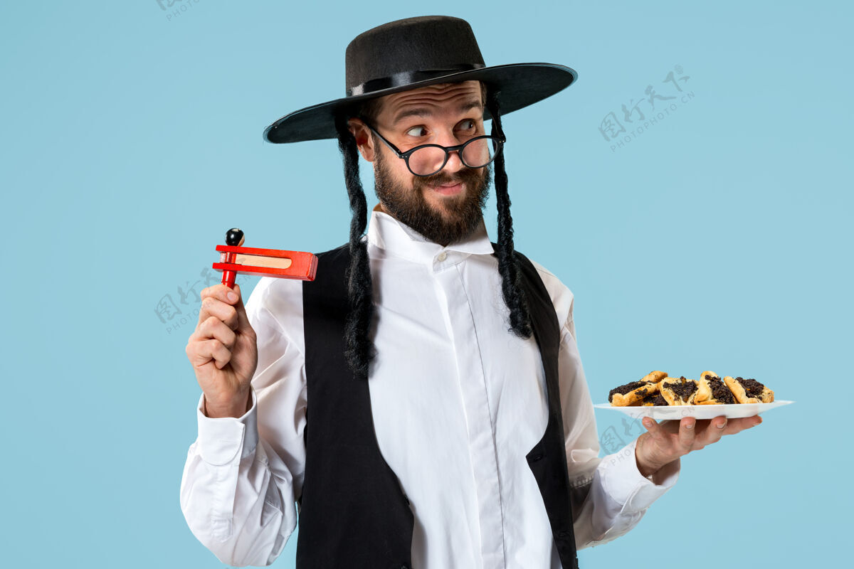 帽子年轻的东正教犹太男子拿着哈曼塔森饼干庆祝普瑞姆节文化罂粟三角形