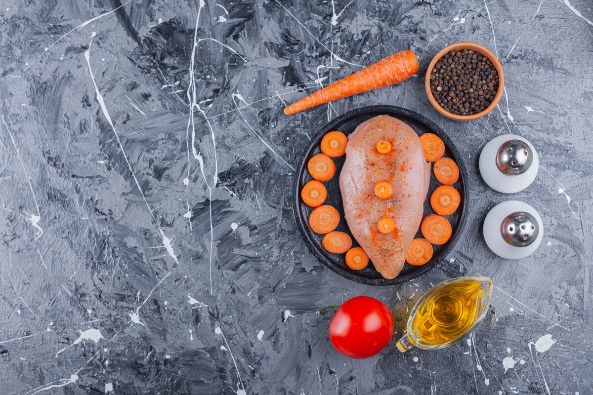 家禽把鸡胸肉和胡萝卜片放在盘子里 在蓝色的表面放上盐 油 香料 胡萝卜和西红柿配料碗蛋白质