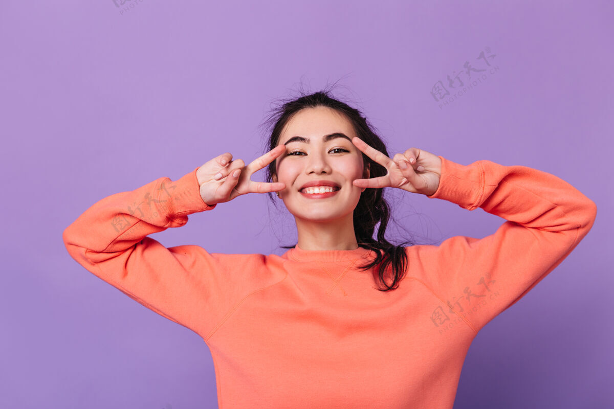 马尾辫快乐的日本女人展示和平的迹象亚洲女模特在紫色背景上微笑着做手势乐趣亚洲女人年轻人