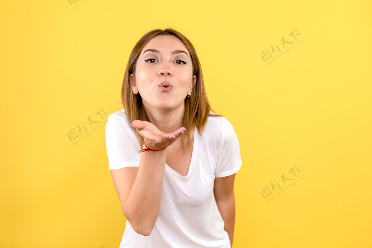 人年轻女子在黄色墙壁上送飞吻的正面图可爱微笑空气
