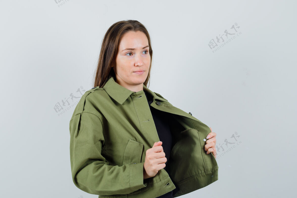 微笑年轻女子拿着她的夹克衫 同时在绿色夹克衫的前视图中向一边看肖像时尚成人