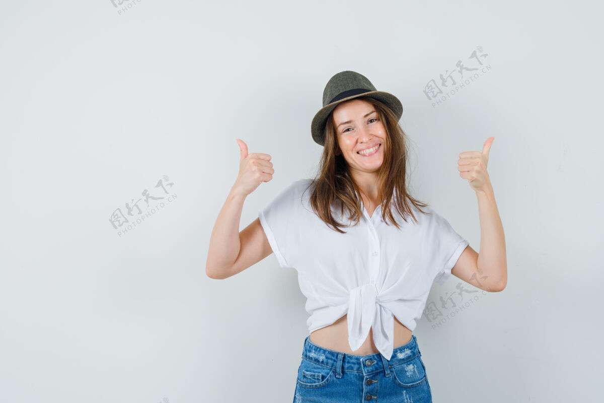 年轻美丽的女士在白色上衣 帽子和拇指上显示快乐 前视图女人成人卷发