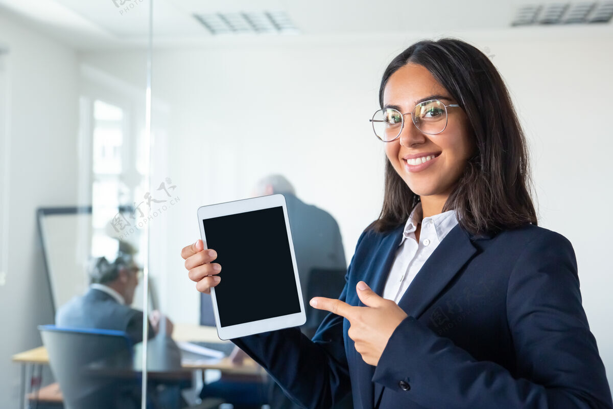 老板快乐自信的商务女士手持平板电脑 手指着空白屏幕 看着相机 微笑着复制空间传播和广告理念律师一起投资者