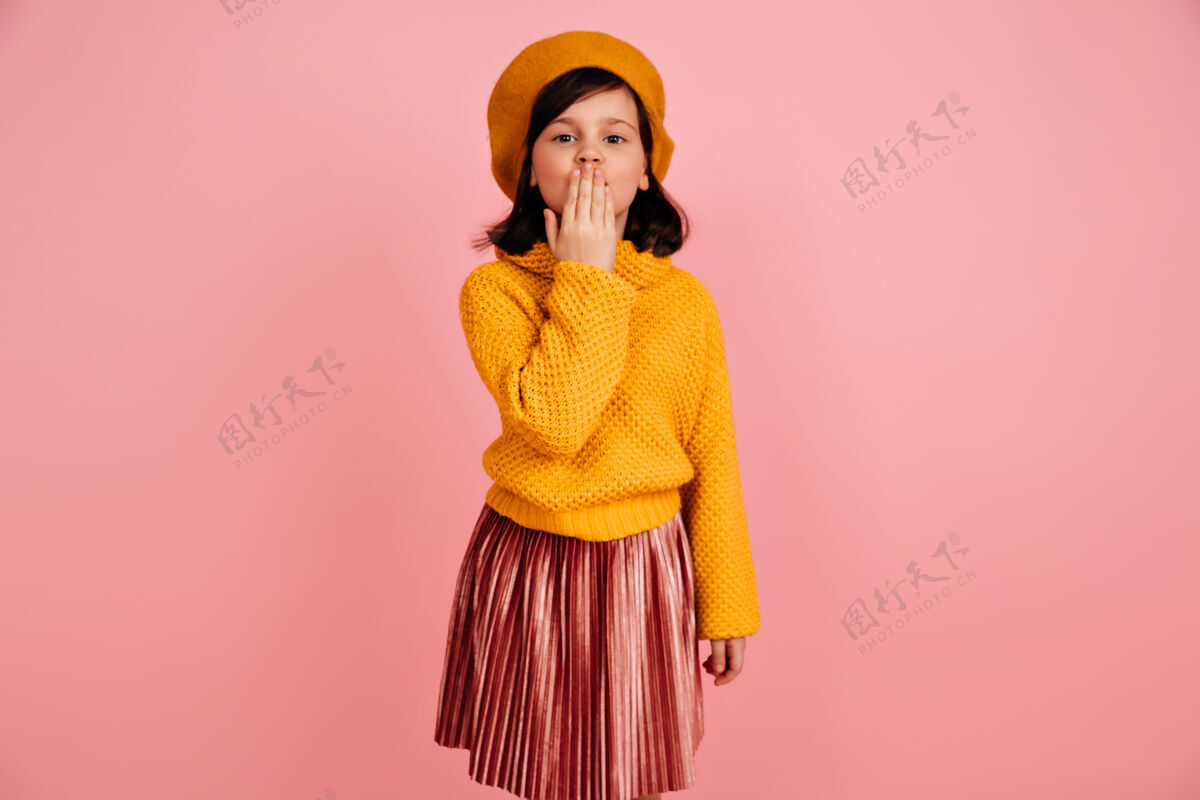 欧洲穿针织衫的未成年少女送空气吻穿着黄色衣服的有趣的孩子粉红色上的孤立贝雷帽童年