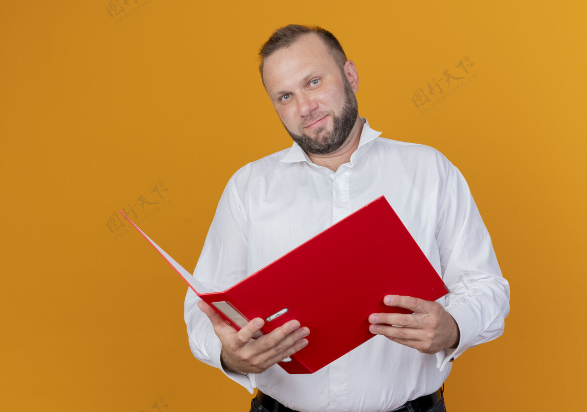 穿留着胡子的男人穿着白衬衫 拿着文件夹微笑着站在橙色的墙上看男人夹