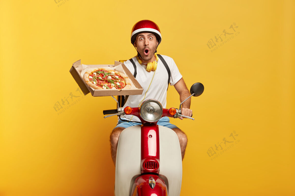 美味惊呆了的英俊男司机骑着摩托车 戴着红色头盔送比萨饼休闲披萨路线