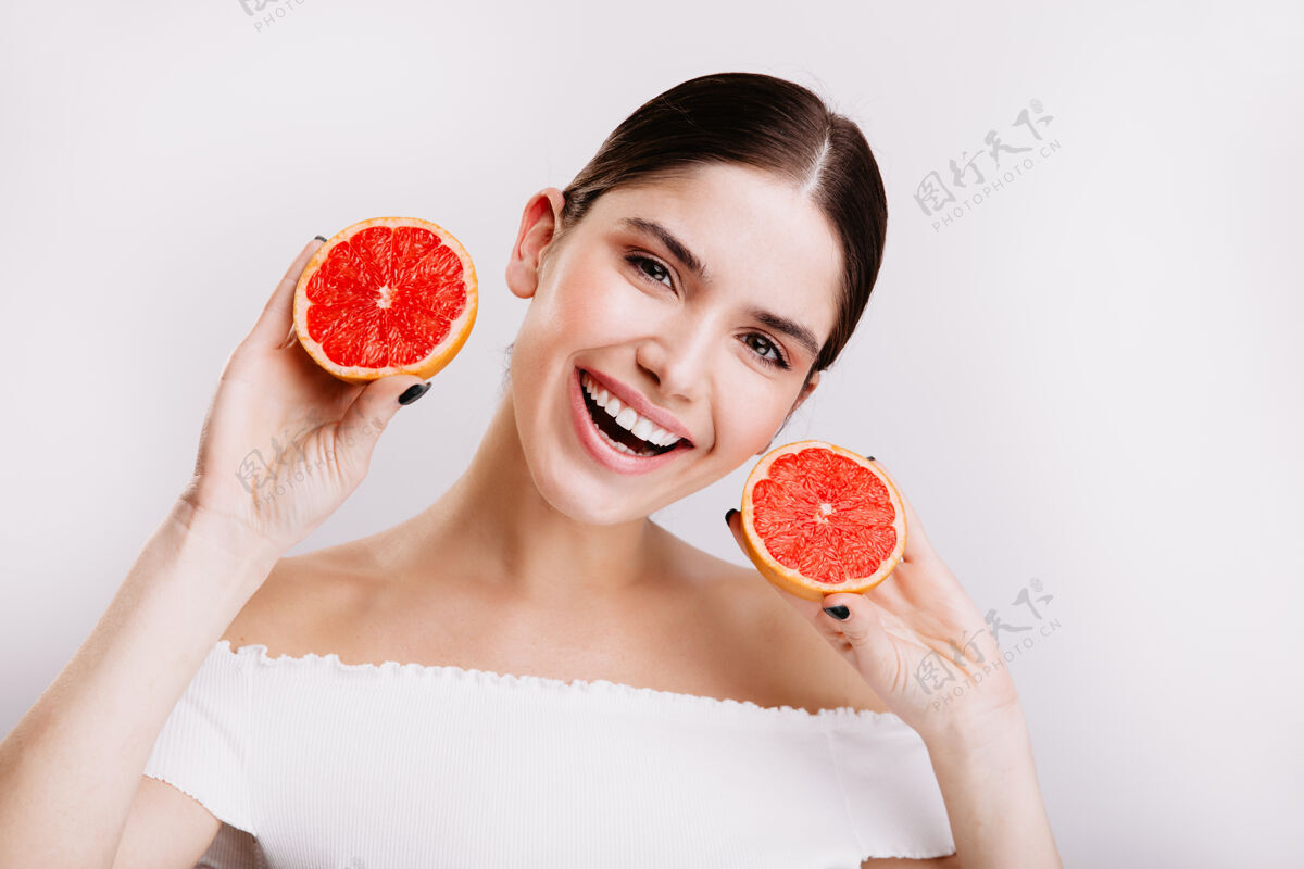 化妆年轻的灰眼睛女孩雪白的微笑 在白墙上展示多汁和健康的葡萄柚快照化妆品柑橘皮肤护理