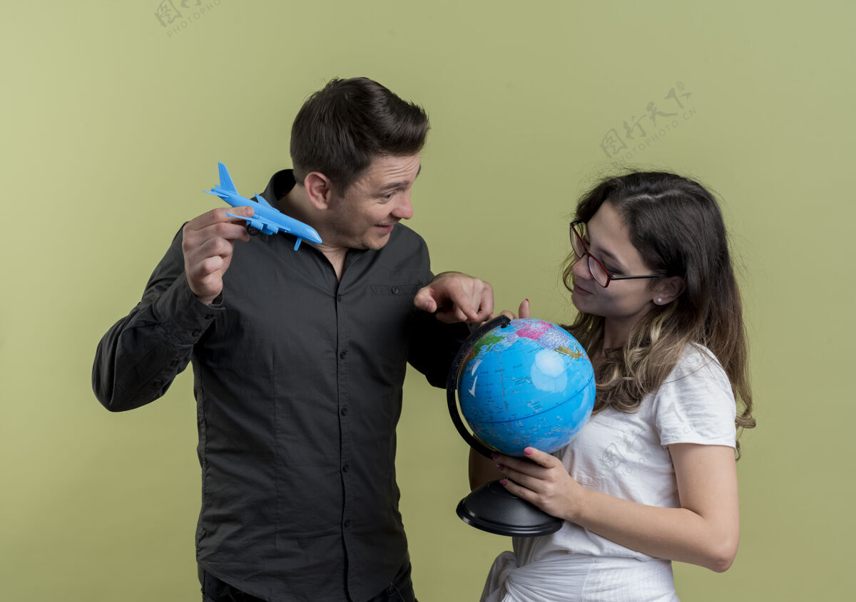 立场一对快乐的年轻游客 一男一女手持地球仪和玩具飞机站在一起 在光墙上玩得很开心举行地球仪空气