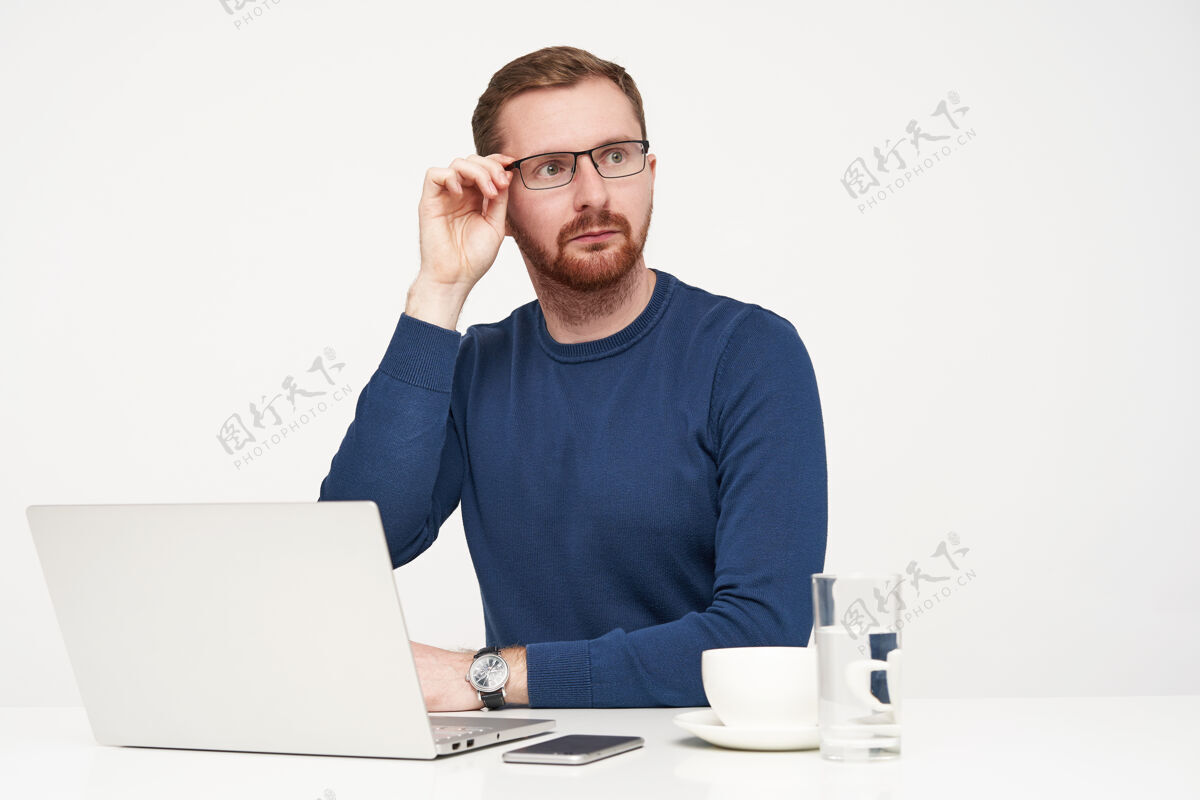 休闲年轻英俊的金发男子惊奇地转过头来 一边惊奇地看着一边 举起手放在眼镜上 坐在白色的背景上白色桌子笔记本电脑