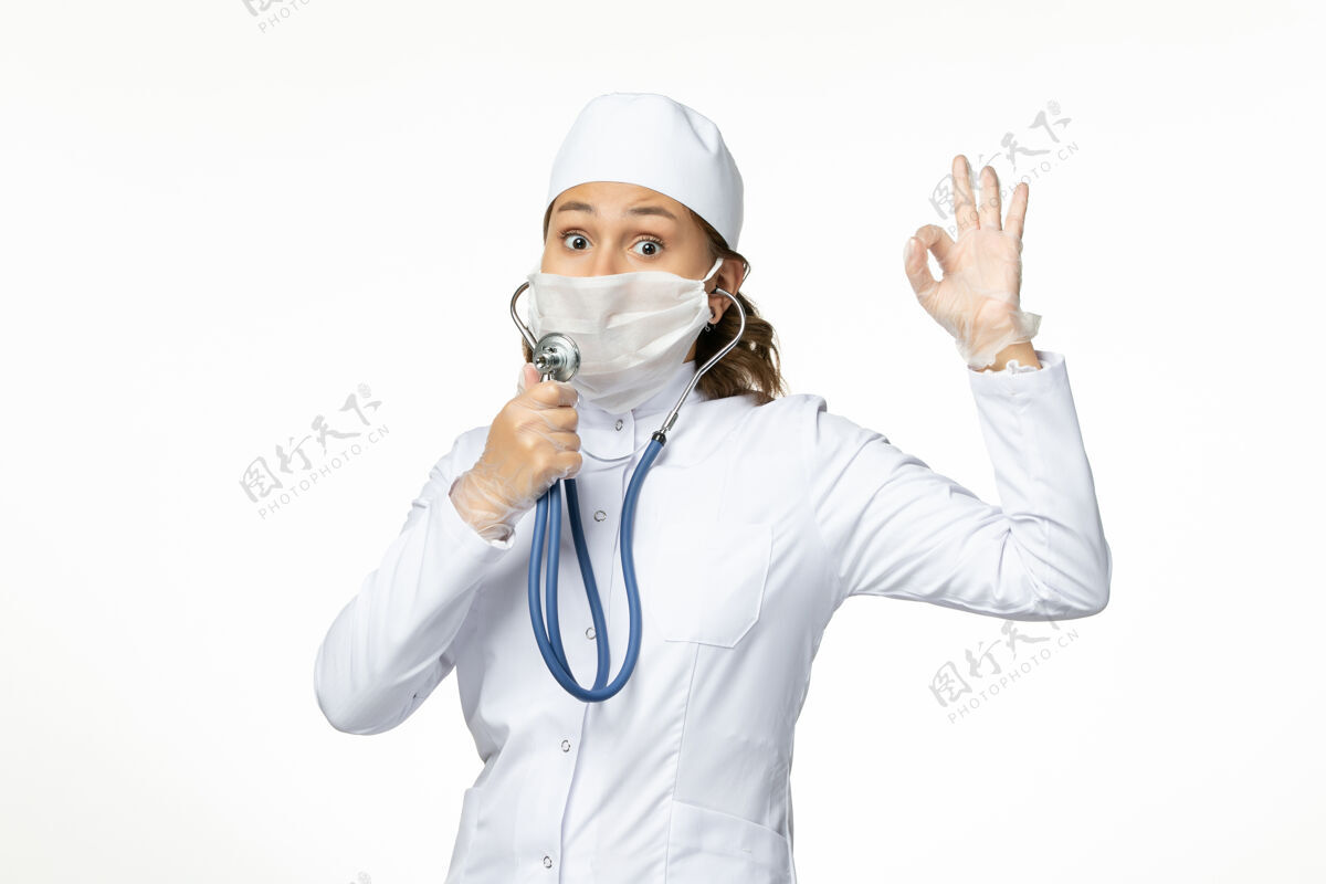 办公桌正面图年轻女医生戴防护无菌口罩因冠状病毒使用听诊器在白色办公桌上女性面罩使用