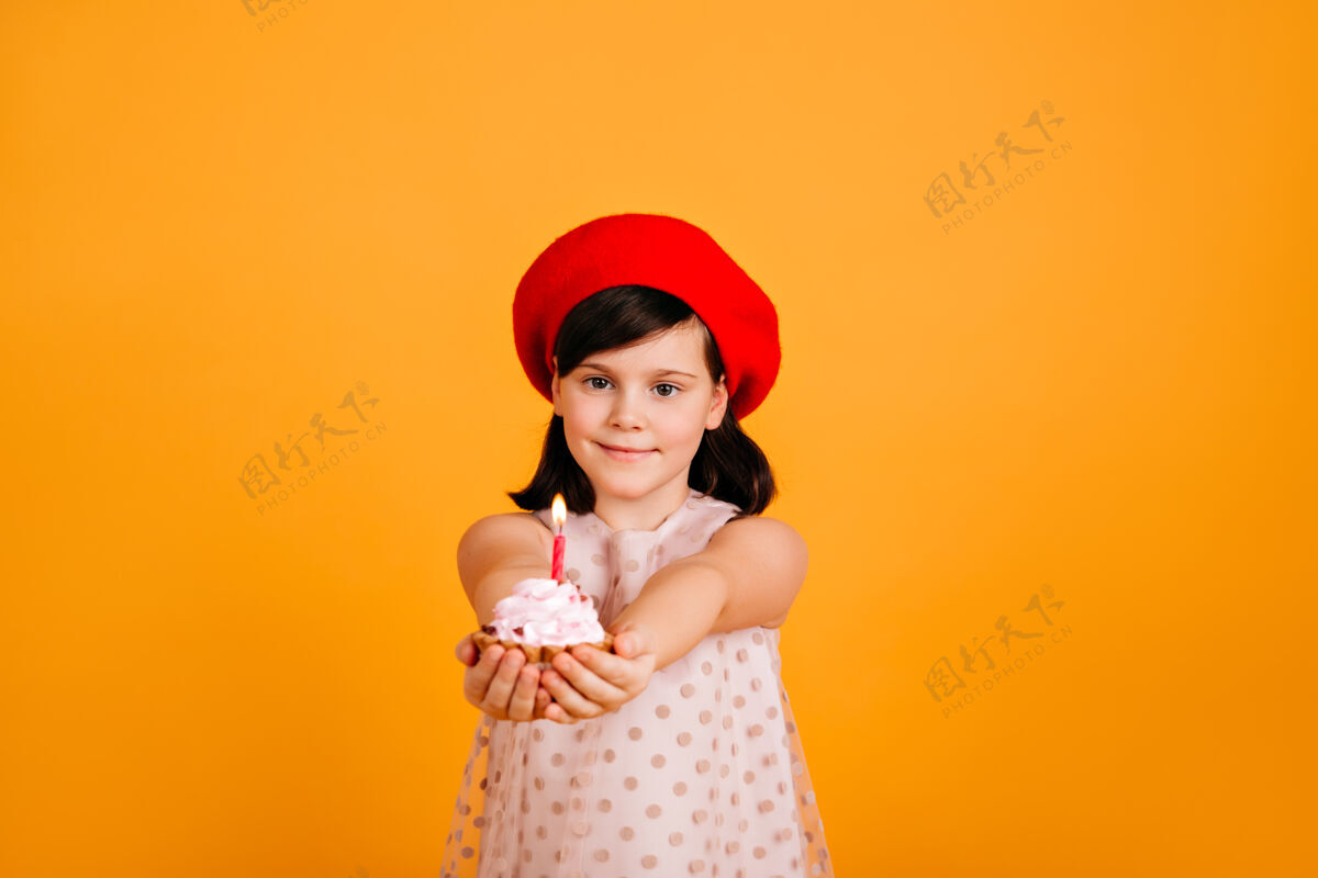 黑发可爱的孩子戴着时尚的贝雷帽庆祝生日高加索女孩儿拿着蛋糕 黄色的墙上孤立着蜡烛欢乐乐趣积极的情绪
