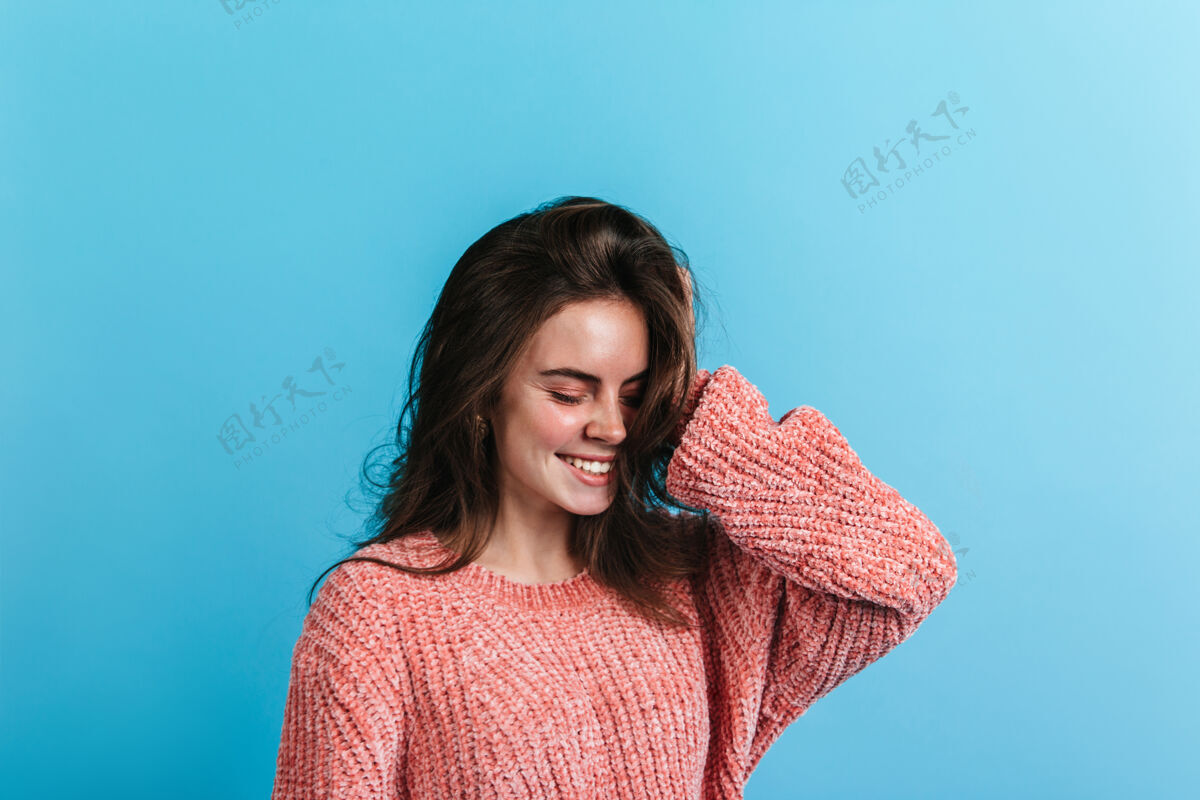 室内穿着粉色毛衣的少女肖像模特闭着眼睛微笑着站在蓝色的墙上完美卷发脸